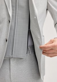 Jasnoszary żakiet z kontrastującą szarością wewnętrzną, z zamkiem błyskawicznym i dwiema przednimi kieszeniami. Materiał ma gładką teksturę z subtelnymi wzorami.
