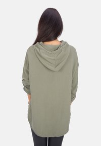 Olivegrüner, leichter Baumwollhoodie mit strukturierter Oberfläche, langen Ärmeln und lockerer Passform. Verfügt über eine Kordelzugkapuze und seitliche Taschen.