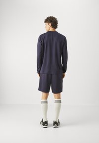 Maglietta sportiva a maniche lunghe color navy e pantaloni corti, con calze bianche fino al ginocchio con strisce nere, abbinate a scarpe da ginnastica nere. Design minimalista.