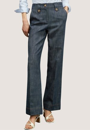 Blauwe pijpenbroek met rechte pijpen en fijne krijtstreep, met een knoopsluiting aan de voorkant, gedragen met witte sandalen met hak en een lichtblauw overhemd.