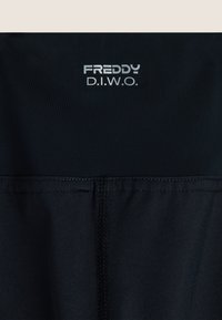 Abbigliamento sportivo nero realizzato in un materiale liscio e elastico. L'elastico della vita presenta il logo "FREDDY" in argento, con cuciture piatte e un design aderente.