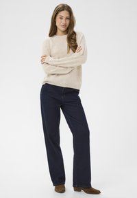 Beige kötött pulóver hosszú ujjakkal, sötétkék, bő szárú farmernadrággal párosítva. Barna bokaig érő csizmák egészítik ki a szettet. Egyszerű és laza stílus.