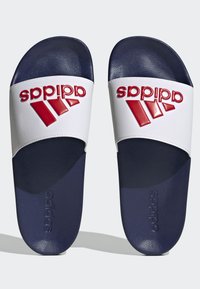 Chanclas Adidas con tira blanca y logo rojo, suela azul marino, material texturizado y forma plana.