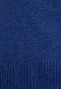 Niebieska dzianinowa tkanina swetra o gładkiej fakturze z prążkowanym obrzeżem. Jednolity kolor i widoczne drobne włókna na całej powierzchni.