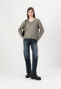 Grå strikket v-hals genser med avslappet passform, kombinert med mørkeblå rette jeans og svarte platåsko. Liten svart skulderveske.