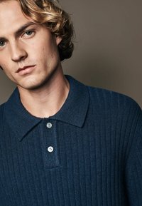 Dunkelblaues geripptes Poloshirt mit strukturiertem Kragen, das über zwei Knopfschlüsse verfügt und eine subtile Textur im Stoff aufweist.