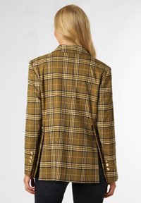 Blazer à carreaux dans des tons de marron, jaune et noir ; possède un col standard et des accents de poignet à quatre boutons ; tissu texturé avec une forme structurée.