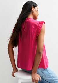 Fuchsia blouse met rimpels op de mouwen, sleutelgat detail op de rug, lichtgewicht stof, gecombineerd met lichtblauwe jeans. Textuurmateriaal met een zachte afwerking.