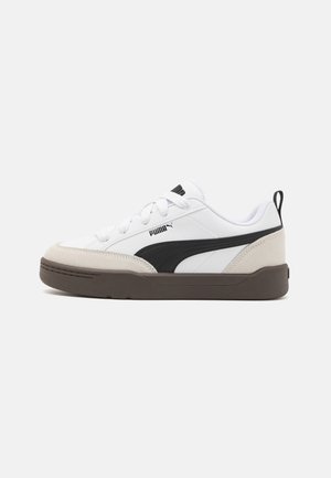 Baskets Puma basses blanches avec bande latérale noire, bout et talon en daim beige, lacets blancs et semelle marron foncé sur fond uni.