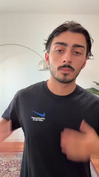 Melnā Nike T-krekls ar zilu logotipu kreisajā krūtīs. Audums šķiet mīksts, standarta piegriezums, ar īsām piedurknēm, to valkā tumšmatains cilvēks.