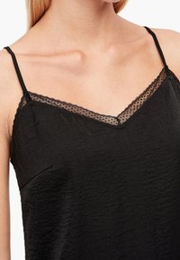 Svart topp med V-ringning och spetskant, tunna justerbara band och krinklad textur. Tyget är lätt och mjukt.