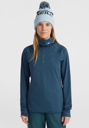Marineblauwe sweatshirt met rits en lange mouwen, voorzien van een hoge kraag, gemaakt van een zachte stof; gecombineerd met een lichtblauwe gebreide beanie met een pompon.