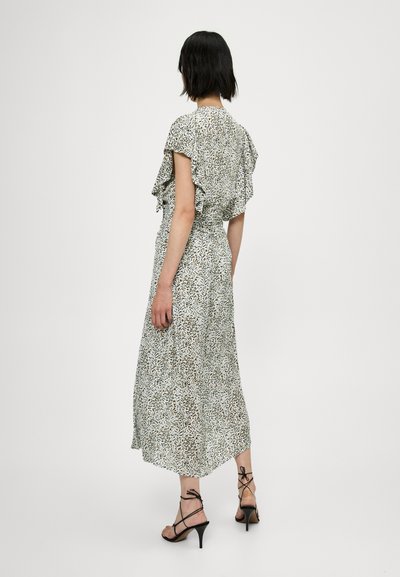 Robe maxi en tissu léger avec un motif abstrait vert, blanc et marron, manches courtes à volants et taille cintrée, associée à des talons noirs à lanières.