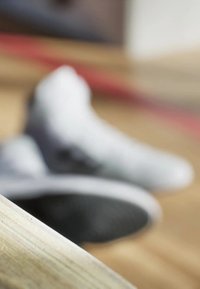 White athletic shoes with a textured sole and contrasting black accents, partially blurred in the background, resting near a light wooden surface.