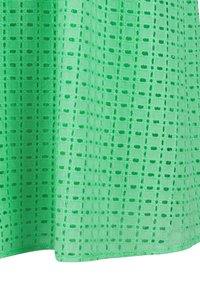 Tissu vert avec un motif de découpes carrées et ovales créant une texture de dentelle en forme de grille.