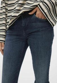 Tumši zili džinsi ar nelielu stiepšanos, kuriem ir cieša piegriezuma un priekšējā kabata. Apvienoti ar svītrainu trikotāžas krekls ar garām piedurknēm.