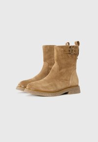 Sandfarbene Wildleder-Ankle Boots mit rundem Zehenbereich, strukturiertem Zwischensohlenbereich und einer dekorativen Schnalle an der Seite. Die Sohle ist leicht erhöht.