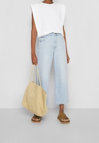 Top sin mangas blanco con canalé, jeans de pierna ancha azul claro, bolso de tote de ante color beige y sandalias marrones de tiras con suela gruesa.