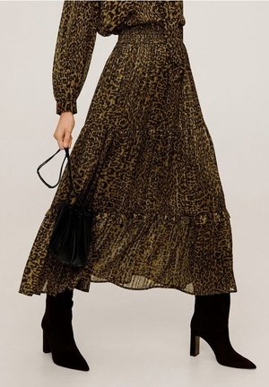 Jupe longue à imprimé léopard associée à des bottines à talons noires et un petit sac à main noir tenu dans la main gauche.