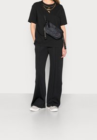 Svart oversized t-shirt, svarta vida byxor, grå sneakers och en mönstrad svart axelväska med en stilren rem. Guldhalsband i lager.