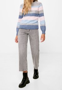 Jersey de punto en rayas pastel de rosa, azul y gris, combinado con unos vaqueros de pierna recta en gris claro y botas negras de cordones hasta el tobillo.
