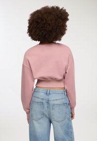 Sweatshirt rosa corto con maniche lunghe, scollatura rotonda e orlo a costine; abbinato a jeans in denim azzurro chiaro a vita alta.