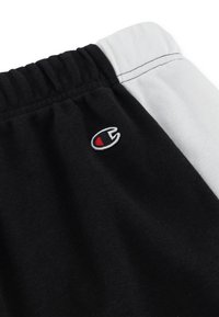 Black and white jogger shorts featuring a ribbed waistband, soft cotton fabric, and a small embroidered logo in red and white.