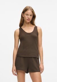 Top din bumbac maro cu margine rotunjită, prezentând un broderie discretă a logo-ului, asortat cu pantaloni scurți. Textură netedă și croială lejeră.