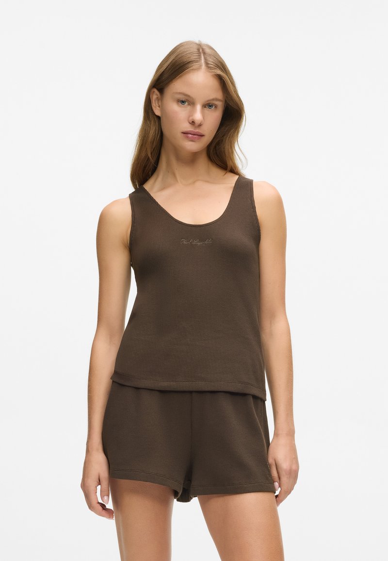 Top din bumbac maro cu margine rotunjită, prezentând un broderie discretă a logo-ului, asortat cu pantaloni scurți. Textură netedă și croială lejeră.