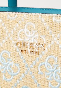 Woven straw handbag with light blue embroidered pattern and metallic gold "GUESS EST. 1981" logo. Features a turquoise interior lining.
