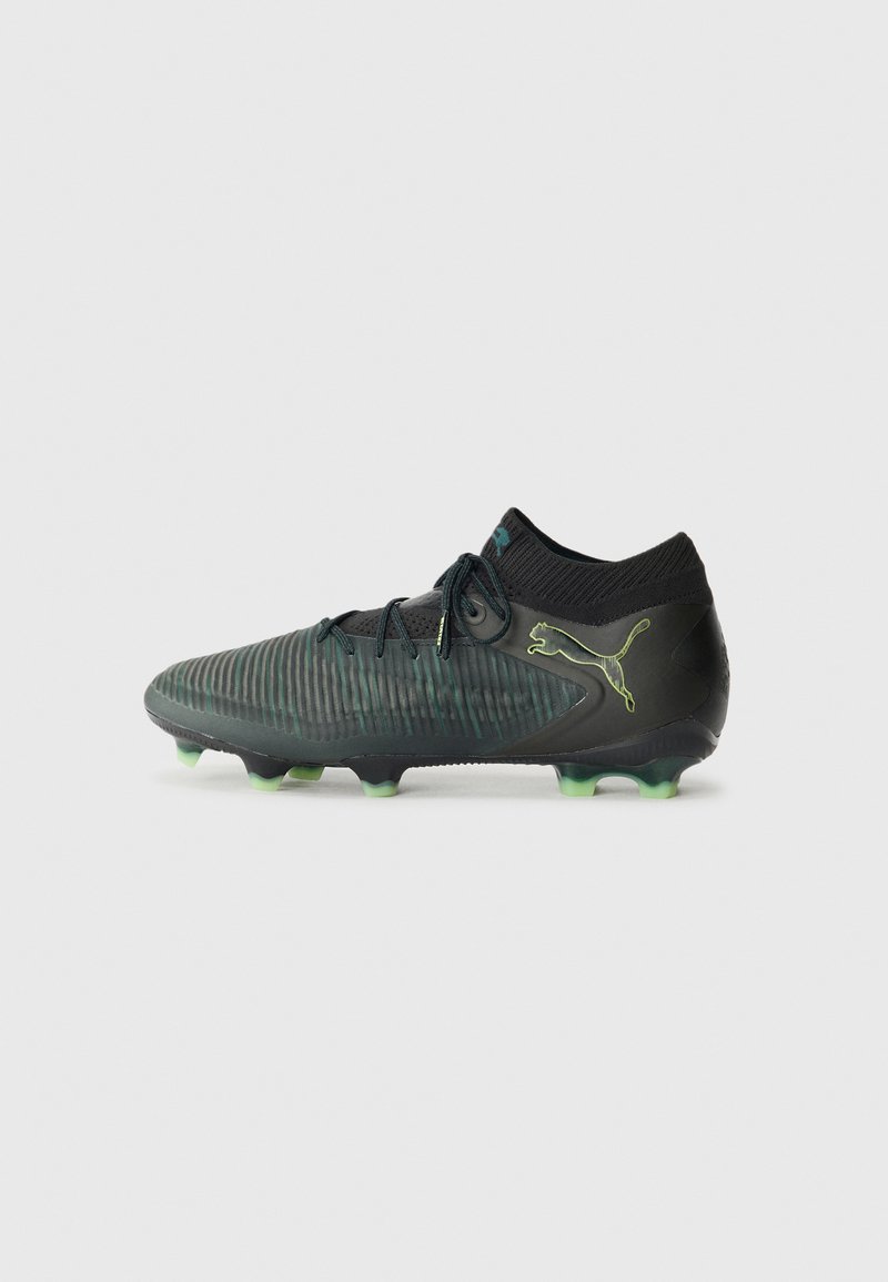 Svart och grön fotbollssko med en texturerad ovandel, ribbat mönster, snörning framtill och fyra gröna dobbar på varje sula. Puma-logga på sidan.