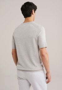 Suéter de punto corto en color gris claro con cuello redondo y dobladillo acanalado. Presenta una textura suave y un diseño de mangas raglán.