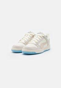 Białe sneakersy z beżowymi zamszowymi akcentami, perforowanym noskiem, jasnoniebieską gumową podeszwą i sznurowaniem. Logo marki na języku i boku.