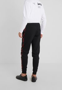 Schwarze Jogginghose mit schmal zulaufender Passform, mit roten Logostreifen an den Seiten und einem elastischen Bund für Komfort. Baumwollstoff.