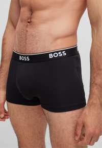 Črne bombažne bokserice s prilegajočim oblikovanjem in elastičnim pasom z blagovno znamko, na katerem je belo napisano "BOSS", z gladko teksturo.