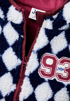 Fliisjakk tumesinise ja valge rombimustriga, millel on burdgundy tõmblukk ja brodüüritud "93" koos "JoJo" detailiga.