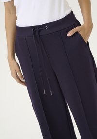 Pantalon de jogging bleu marine avec taille élastique à cordon de serrage, poches latérales et coupe décontractée. Tissu lisse avec des plis verticaux pour plus de détails.
