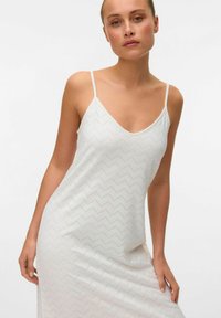 Witte mouwloze jurk met V-hals, zigzagpatroon en lichtgewicht stof met subtiele textuur. Benadrukt een getailleerd silhouet.