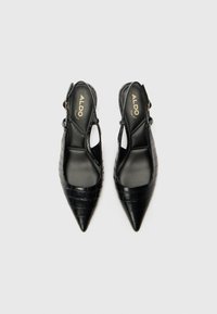 Tacones altos negros tipo slingback con punta afilada, patrón de cocodrilo en relieve y un forro interior suave. Logo de la marca visible en las plantillas.