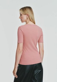 Różowa, dopasowana koszulka z krótkim rękawem i okrągłym dekoltem, wykonana z prążkowanego materiału, zestawiona z czarnymi skórzanymi spodniami. Subtelna tekstura podkreśla wygląd tkaniny.