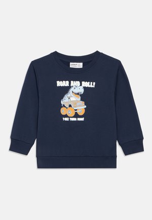 Mørkeblå hettegenser laget av bomull, med et dinosaurmotiv og en lastebil med store hjul. Teksten sier "RÅLE OG RULLE! LAG TURBOLYD!"