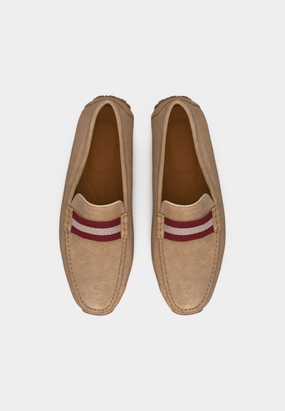 Mocassins en daim beige avec des bouts carrés arrondis et une bande en tissu décorative rayée rouge et blanche sur le dessus.