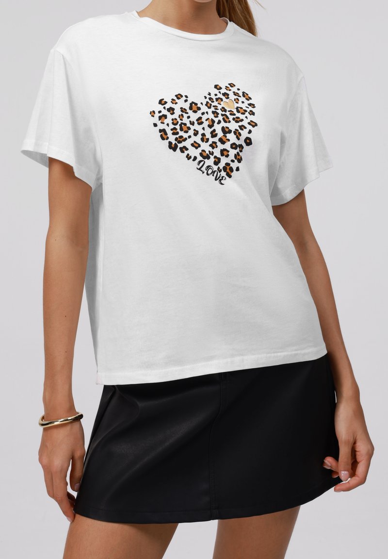 Woman wearing white t-shirt with leopard print heart and word "love," paired with a black leather skirt and gold bracelet.