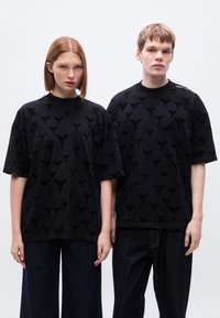 Μαύρα μπλουζάκια με ανάγλυφο σχεδιασμό και διακριτικά μοτίβα. Χαλαρή γραμμή, κοντά μανίκια, συνδυασμένα με σκούρο μπλε τζιν παντελόνια με φαρδιά μπατζάκια.