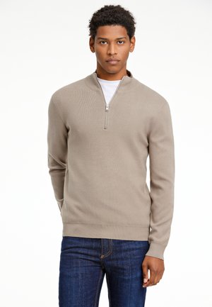 Maglione beige con collo zip, maniche lunghe, polsi e orlo a costine, abbinato a jeans blu scuro. Il maglione ha una texture liscia e una vestibilità classica.
