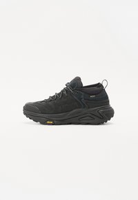 Chaussure de randonnée noire avec une tige en suède texturé et en maille, semelle en caoutchouc proéminente et logo Vibram sur la semelle extérieure. Vue de profil montrée.