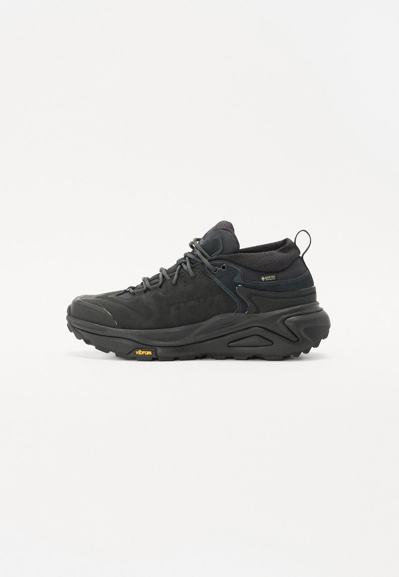 Chaussure de randonnée noire avec une tige en suède texturé et en maille, semelle en caoutchouc proéminente et logo Vibram sur la semelle extérieure. Vue de profil montrée.