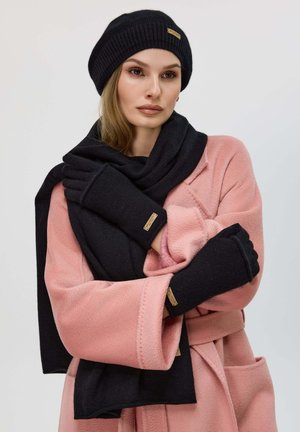Berretto di lana nera, sciarpa coordinata e guanti senza dita abbinati a un morbido cappotto rosa. Presenta un tessuto testurizzato e dettagli in tonalità beige.