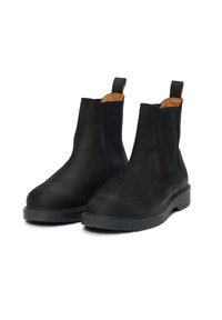 Černé semišové kotníkové boty s elastickými bočními panely, táhly na obouvání a texturovanou černou gumovou podešví. Hladký povrch s hnědým vnitřním prošíváním.