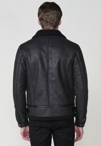 Giacca nera con finitura testurizzata, colletto in shearling e bordatura in pelle all'orlo. Presenta maniche lunghe e polsini abbottonati.